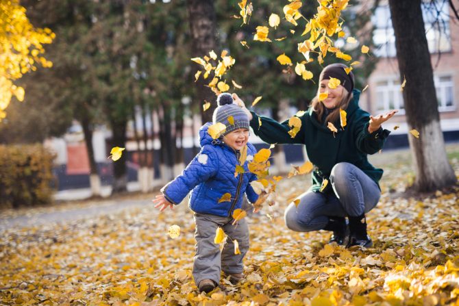 dećak se sa mamom igra sa jesenjim lišćem